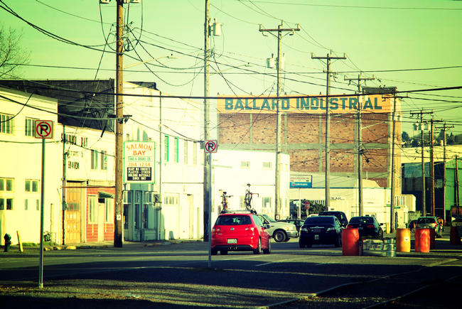 A retro looking photo of a street in an industrial area with a red car in the center of the image
